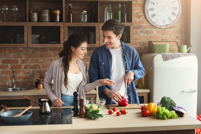 A happy couple cooking dinner at home in their own kitchen to save lots of money on their grocery bill and food budget.