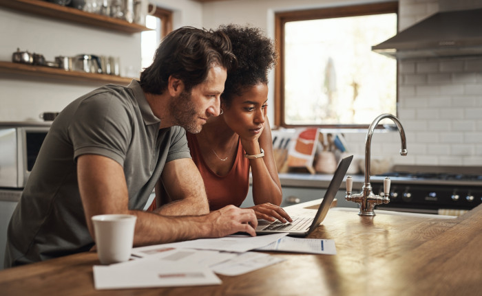 A couple budgeting together on a laptop computer in their kitchen.